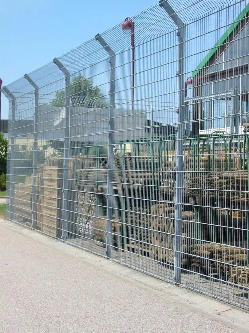 Hoher Stahlgitterzaun mit abgewinkelten Auslegern und Drahtreihen am oberen Zaunabschluss
